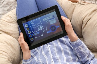 Evde elinde tablet bilgisayarı olan bir kadın teslimat hizmeti başvurusunun açık sayfasını tutuyor