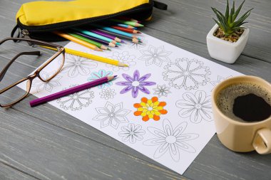 Renkli resim, bardaklar, bir fincan kahve ve tahta arka planda kalemler.