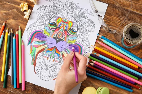 Woman coloring picture at wooden table, closeup