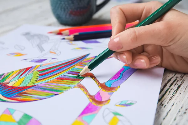 Woman coloring picture at wooden table, closeup