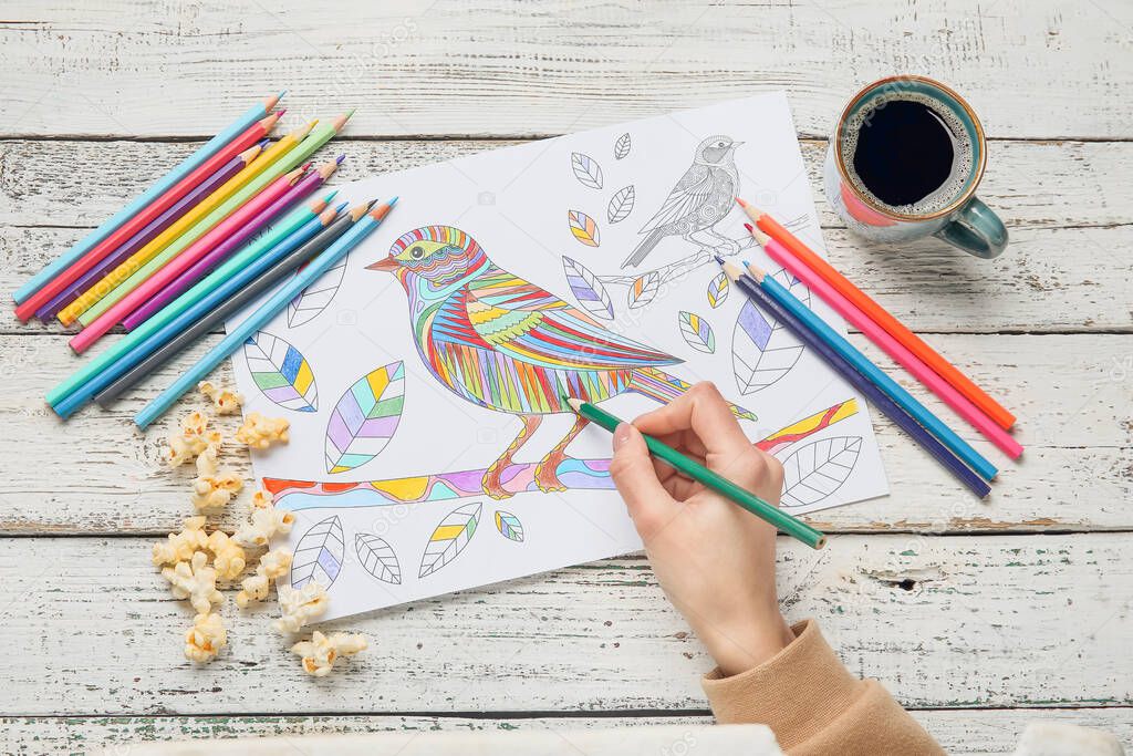 Woman coloring picture at wooden table, closeup