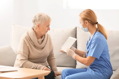 Tablet bilgisayarı olan bir doktor ve evde yaşlı bir kadın.