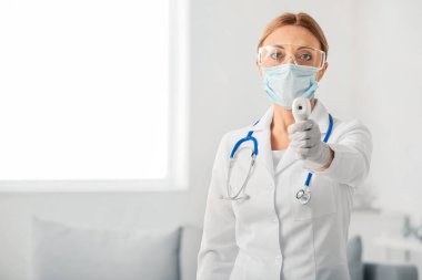 Kadın doktor portresi koruyucu üniformalı ve kızılötesi termometresi kapalı.