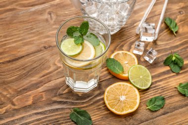 Bir bardak sağlıklı limonata, buz küpleri ve ahşap arka planda narenciye meyveleri.