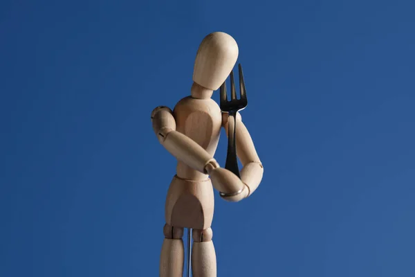 Wooden mannequin with fork on color background