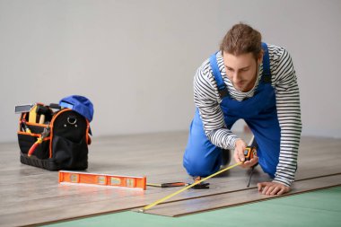 Marangoz odada lamine döşeme ölçümleri yapıyor.