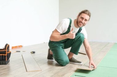 Marangoz, odaya lamine döşeme montajı sırasında baş parmağını kaldırdığını gösteriyor