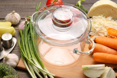 Şık bir tencere ve ahşap arka planda taze sebzeler.