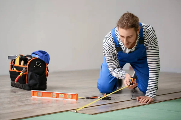 Marangoz odada lamine döşeme ölçümleri yapıyor.