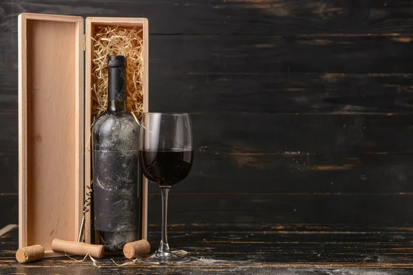 Box with bottle of wine and glass on dark wooden background