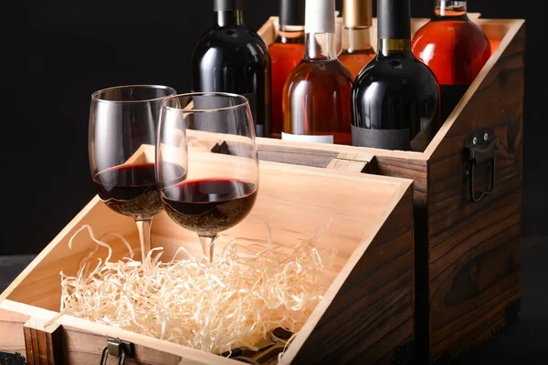 Box with bottles of wine and glasses on dark background