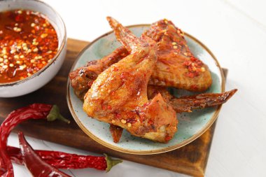 Lezzetli kızarmış tavuk kanatları, kuru kırmızı biber ve hafif ahşap arka planda sıcak bal.