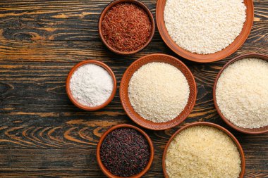 Ahşap zemin üzerinde farklı tipte çiğ pirinç bulunan kaseler.