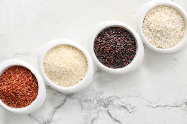 Açık arkaplanda farklı tipte çiğ pirinç bulunan kaseler