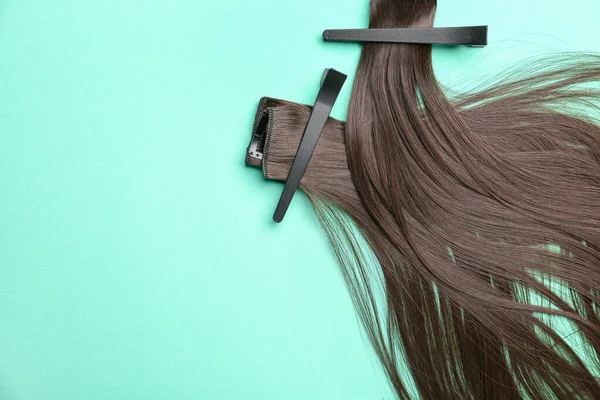 Strands of brunette hair with clips on color background