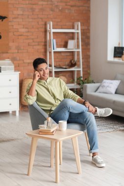 Genç Afro-Amerikalı adam evdeki koltukta oturuyor.