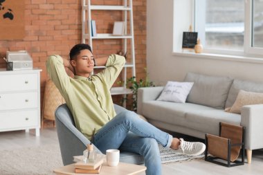 Genç Afro-Amerikalı adam evdeki koltukta oturuyor.