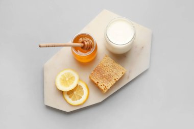 Tatlı ballı cam kavanoz, limon dilimleri, gri arka planda tarak ve süt.