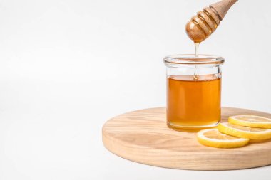 Tatlı bal, beyaz arka planda cam kavanoza damlıyor.