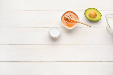 Tatlı bal, avokado, bir sürahi süt ve hafif ahşap arka planda kozmetik ürünü.