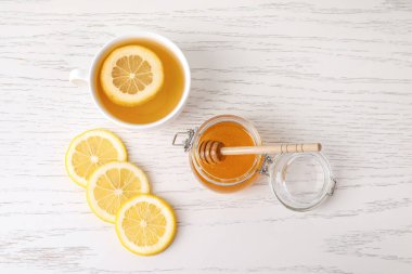 Tatlı ballı cam kavanoz, bir fincan çay ve arkaplanda limon dilimleri.