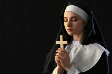 Young praying nun on dark background clipart