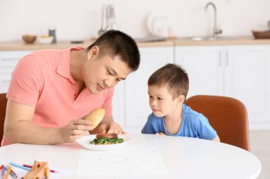 Baba küçük oğlunu mutfakta besliyor.