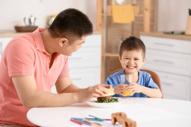 Baba küçük oğlunu mutfakta besliyor.
