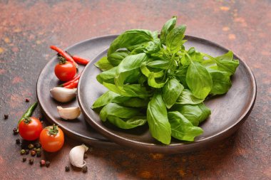 Taze fesleğen yapraklı tabaklar, baharatlar ve arkaplanda domatesler.