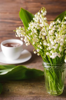 Vadideki güzel zambak çiçekleri ve ahşap arka planda bir fincan çay.