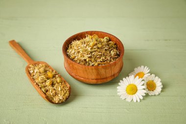 Kurumuş papatya çiçekleri ile renkli ahşap arka planda kase ve kepçe