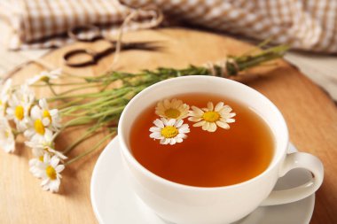 Bir fincan lezzetli papatya çayı ve çiçekler masada, yakın plan.