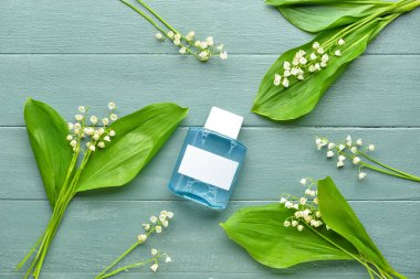 Bir şişe parfüm ve gri ahşap arka planda vadideki zambak çiçekleri