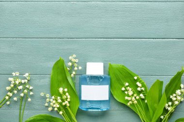 Bir şişe parfüm ve gri ahşap arka planda vadideki zambak çiçekleri