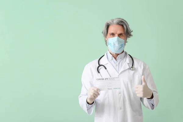 Doctor with International Certificate of Vaccination showing thumb-up on color background