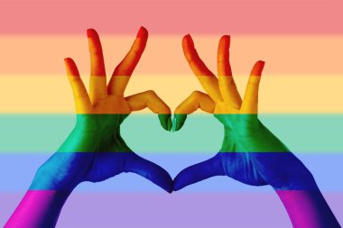 Elleriyle gökkuşağı arkaplanına LGBT bayrağı renginde kalp yapan kadın