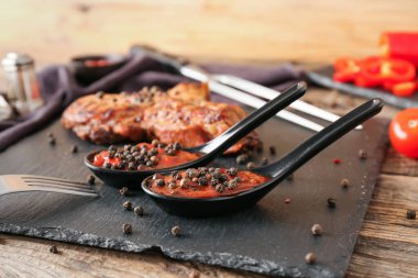 Biber soslu kaşıklar ve ahşap arka planda kızarmış et, yakın plan.