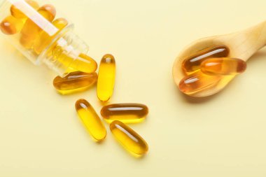 Renk arka planında balık yağı kapsülleri olan şişe ve kaşık