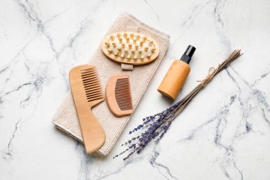 Saç tarakları, masaj fırçası, havlu ve arka planda bir şişe kozmetik ürünü.