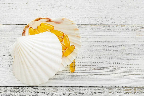 Sea shells with fish oil capsules on light wooden background