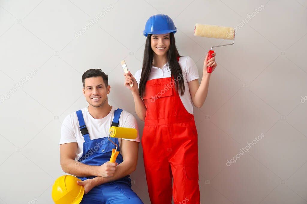 Young couple with rollers and brush on light background