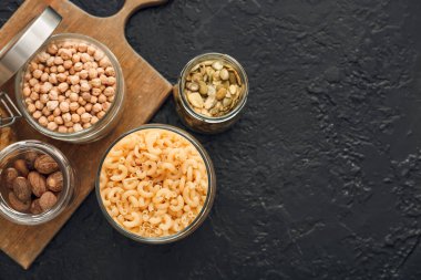 Koyu arkaplanda farklı ürünler olan cam kavanozlar.