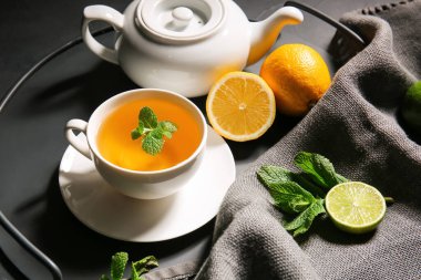 Bir fincan lezzetli yeşil çay, demlik ve malzemelerle dolu bir tepsi.