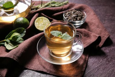 Bir fincan lezzetli yeşil çay ve malzemeler koyu masada.