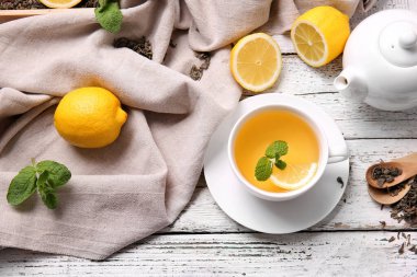 Bir fincan lezzetli yeşil çay, demlik ve hafif ahşap arka planda malzemeler.