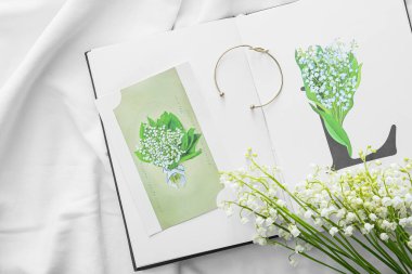 Vadideki güzel zambak çiçekleri, açık kumaş arka planda kitap ve tebrik kartı.