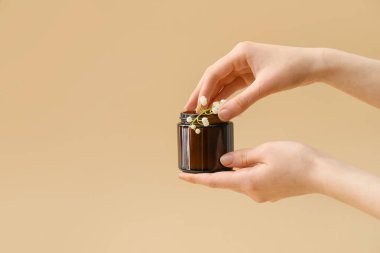 Kadın eli, krema kavanozu ve arka planda zambak çiçeği.