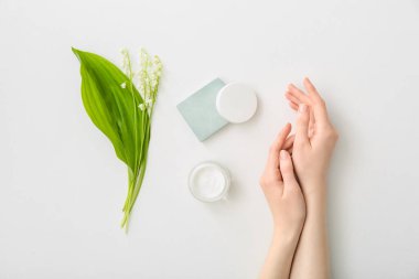 Kadın eli, krema kavanozu ve beyaz arka planda zambak çiçeği.