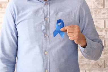 Açık tuğla duvarın yanında mavi kurdeleli bir adam var. Yakın plan. Kolon kanseri kavramı