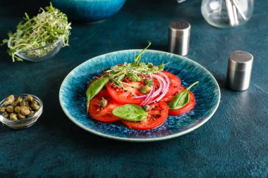 Lezzetli domates carpaccio tabağı, taze lahana ve koyu arkaplanda kapari.